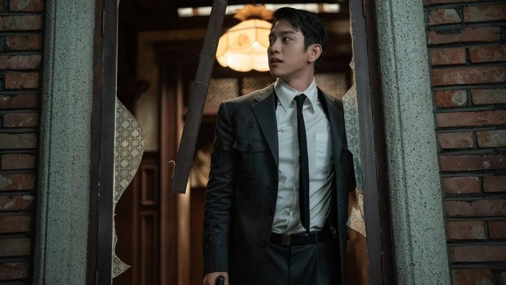Park Jin-young as Sato Hideo standing outside a doorway in 100 Days of Deception