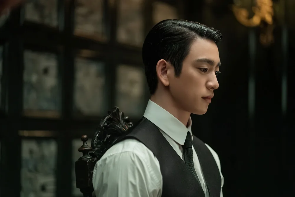 Park Jin-young as Sato Hideo seated indoors in a white shirt and black waistcoat.
